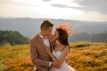 The bride and groom hug and tenderly with each other. Sunset. Wedding photo on a background of autumn mountains. A strong wind inflates hair and dress. Close-up.