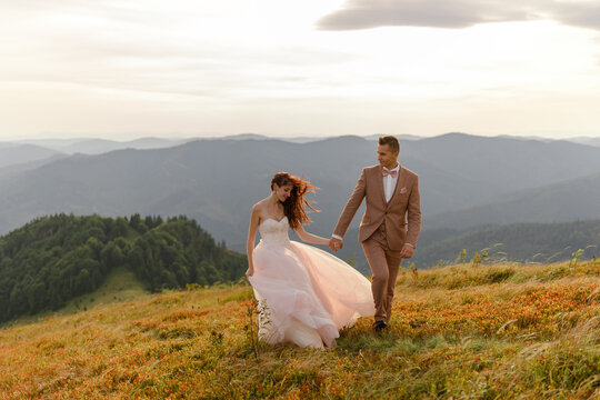 The groom leads the hand of his bride. Sunset. Wedding photography background on autumn mountains. Strong faith inflates hair and dress.