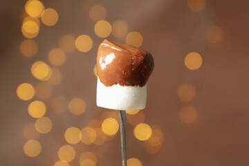 Marshmallow in chocolate against brown background with blurred lights