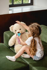 cute child holding toy cup near teddy bear while playing in living room