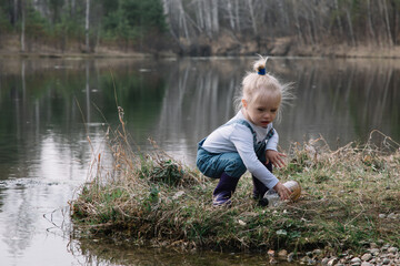 Little girl in rubber boots catches and feeds fish on the river in a jar