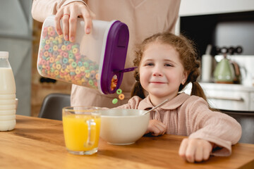 selective focus of mother holding container with tasty corn flakes near bowl and cute daughter