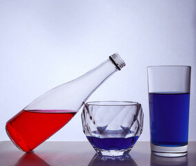 composition from a bottle and glasses with multicolored liquid on a white background. The bottle rests on a glass of whiskey