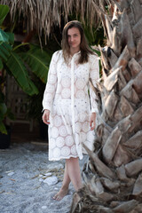 A beautiful brunette girl in white beach dress posing at the beach. Girl standing near palm. high fashion look.top view . Summer