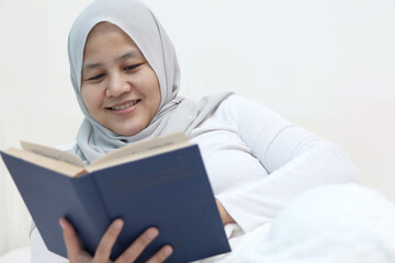 Happy female smiling while reading book on bed, leisure and calming activity of smart people enjoy reading before sleep