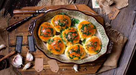 traditional tasty ukrainian baked buns with garlic and dill in oval baking dish on rustic wooden board. overhead shot