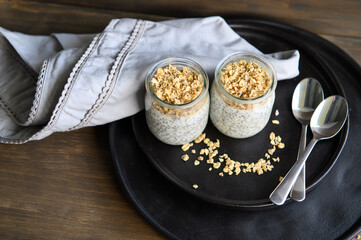 Two small jars with yogurt and chia seeds, granola on a black plate. Healthy breakfast. Selective focus.