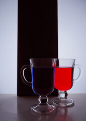 silhouettes of two glasses on a black and white background. Blue and red liquid