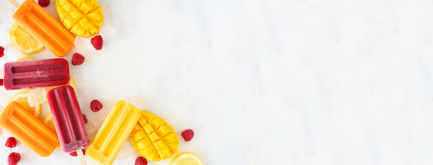 Variety of vibrant summer fruit ice pops. Above view corner border on a white marble banner...