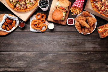 Variety of take out and fast foods. Pizza, hamburgers, fried chicken and sides. Top border. Above view on a dark wood background with copy space.
