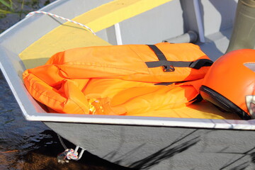 New bright orange life jacket ang orange helmet in alloy boat bow cockpit close up, safety on...