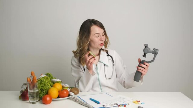 A doctor-nutritionist at his desk conducts online training for his clients by video call over the phone holding an orange. Healthy Eating.