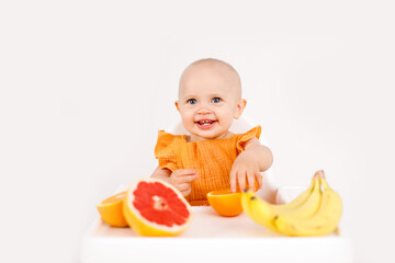 baby girl sitting in a child's chair eating fruit on a white background. baby food concept, space for text