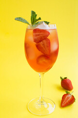 Cocktail drink with strawberry and ice in a wineglass on the yellow  background. Location vertical. Closeup.