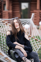 Happy woman in dark shirt, jeans and sunglasses relaxing in hammock in forest at sunset. relaxing concept. Beautiful girl.