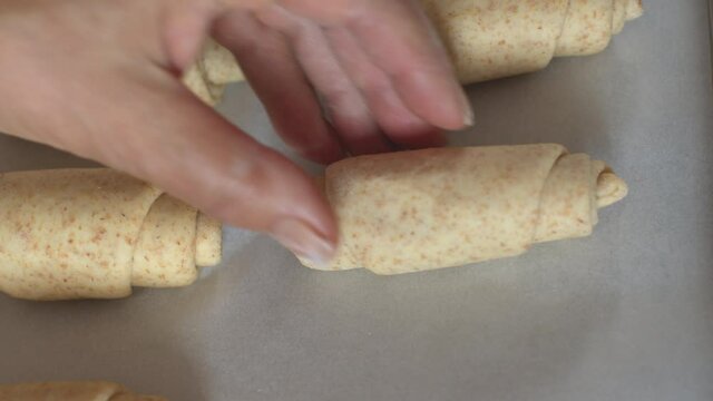 Overhead top view shot of woman hand putting a raw organic whole wheat bread roll or croissant in a baking sheet in the kitchen or at the bakery. Slow-motion.