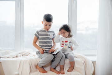 Brother and sister are sitting on the windowsill and reading a book. Happiness, family