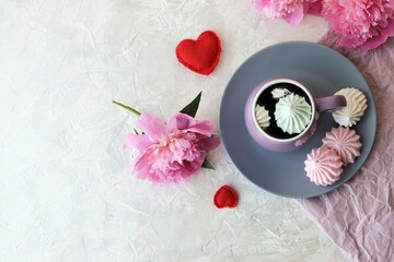 Cup of coffee with meringues, pink peony flowers, hearts on a light background, romantic breakfast concept, top view
