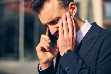 Serious brunette businessman talking on phone outside