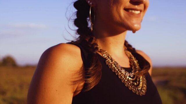 Happy smiling boho girl with golden jewelry looking at sunset