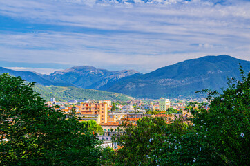 Fototapeta na wymiar Aerial panoramic view of residential quarter of Brescia city and Alps mountain range, green trees foreground, blue cloudy sky, Lombardy, Northern Italy