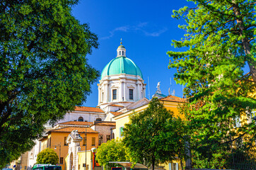 Santa Maria Assunta Roman Catholic church or New Cathedral or Duomo Nuovo building and green tree branches foreground, clear blue sky, Brescia city historical centre, Lombardy, Northern Italy