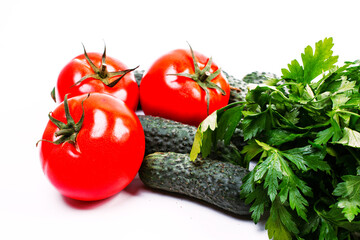 three red tomatoes, cucumbers and parsley on a white background