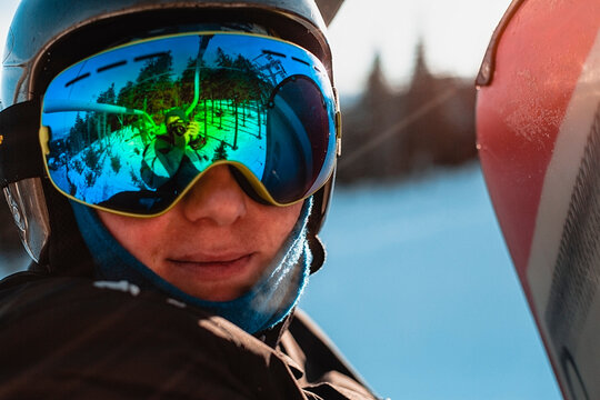 Head and shoulders of person wearing a black helmet and dark goggles on a ski slope.