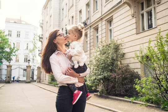 A mother holding her daughter and giving her a kiss in a street setting in Berlin.