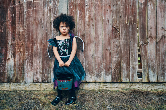 A girl in a Halloween witches costume with a spider painted on her face in costume ready for trick or treating.