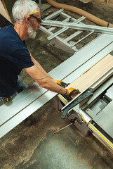 Top view of a carpenter cutting a piece of wood on the electric saw cutting machine in a wood workshop