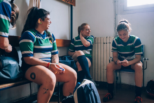 Four women wearing green, blue and white rugby shirts sitting in a changing room.
