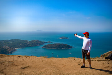The young man shows his hand at the view from the mountain. Sportswear, cap. The Andamand Sea of Phuket Island, Thailand. Tropical exotic island.