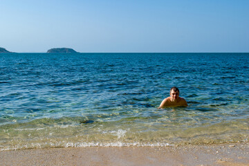 Fototapeta na wymiar A happy young man swim in the sea. Beautiful landscape of exotic white sand sea beach and palm trees Southeast Asia, Thailand.