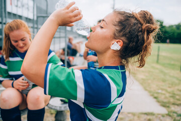 A woman wearing a blue, white and green rugby shirt drinking from a bottle of water