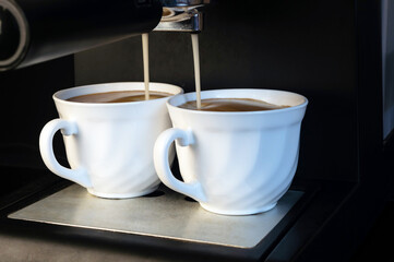 The coffee machine brews strong tasty coffee and pours it into two white mugs on a black background