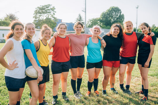 A line of women standing on a pitch with arms around each other and smiling at the camera.