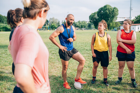 A group of women standing in a circle listening to their male rugby coach.