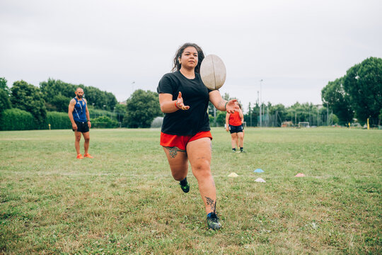 Rugby training, woman catching a rugby ball with others waiting behind and coach standing to the side.