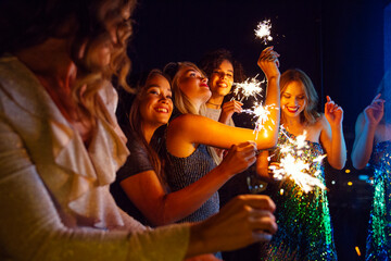 Five women dressed to go out for the evening standing outside with sparklers.