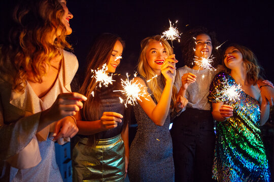 Five women dressed to go out for the evening outside with sparklers.
