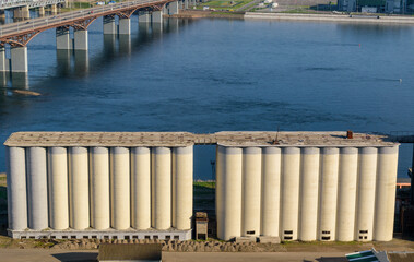 Old Grain elevator by the river. A agrarian facility complex designed to stockpile. High concrete structure. Road bridge, water.