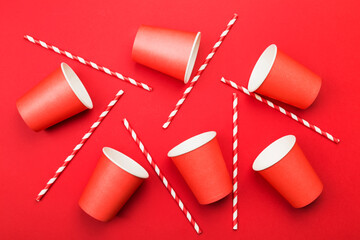 Red paper cups and red-white straw on red background. Top view