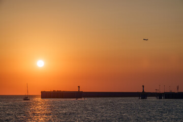 Beautiful red and orange sunset over the sea. The sun goes down over the sea. Silhouette of a take-off airplane and the setting sun. Silhouette of sea port at sunset