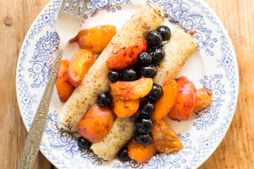Morning breakfast with french crepes, blueberry and apricot in caramel on a plate on wooden table background. Top view.