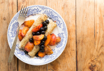 Morning breakfast with french crepes, blueberry and apricot in caramel on a plate on wooden table background. Top view.