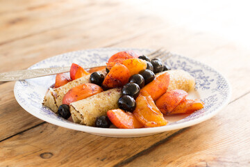 Morning breakfast with french crepes; blueberry and apricot in caramel on a plate on wooden table background. Side view.