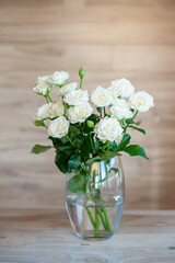 White sweet roses in soft light on a wooden background in a glass transparent vase.