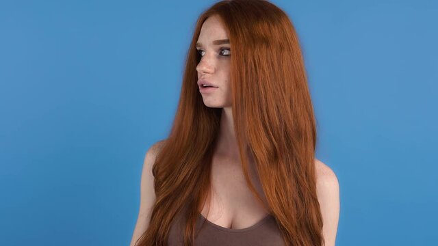 Young ginger woman in brown shirt. She looking annoyed and showing blah blah blah sign while posing against blue studio background. Close up