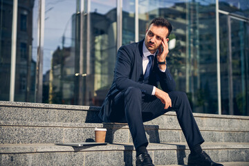 Concentrated brunette man sitting outside alone with gadget